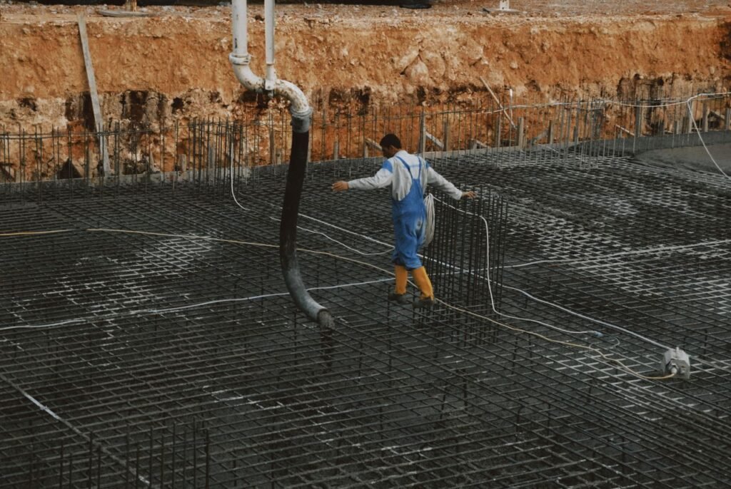 A construction worker in yellow boots walks on rebar grid at a building site.